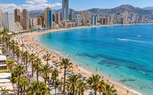 The Levante beach curving past a wall of apartment towers, with the Serra Gelada hills behind